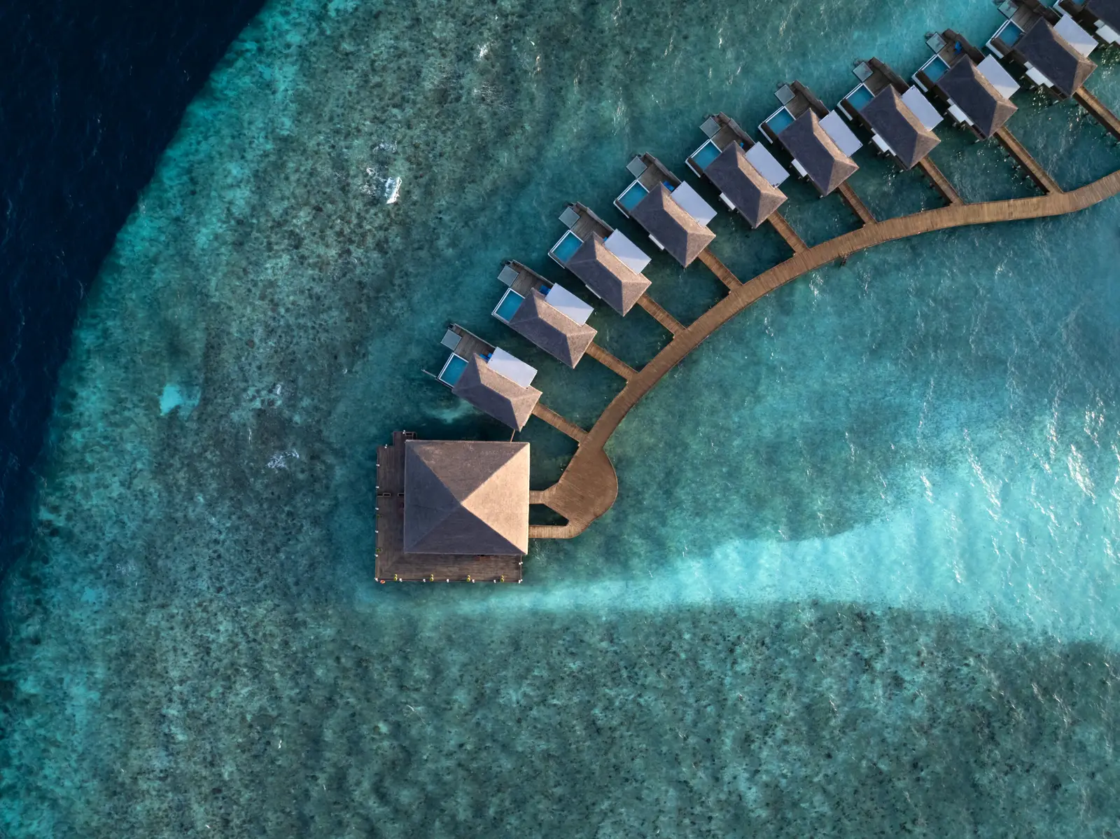 The arc of water villas from above, over the reef and the lagoon.