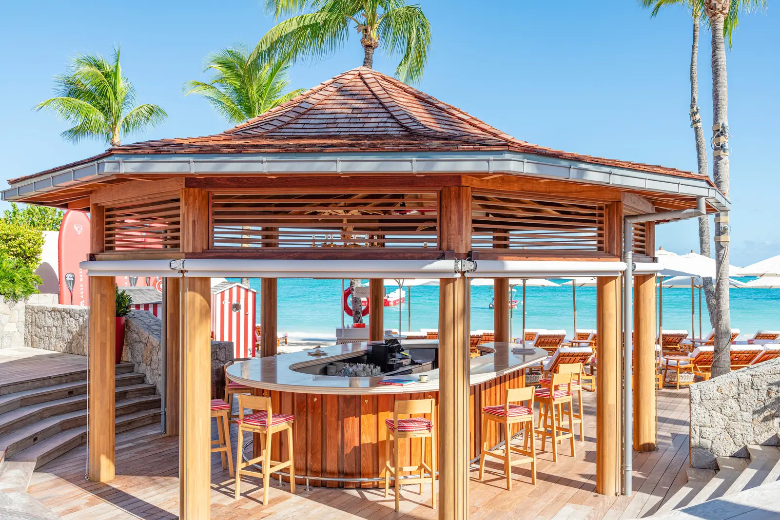 The Beach Bar’s octagonal timber pavilion, with stools at the counter, palms and the sea behind.