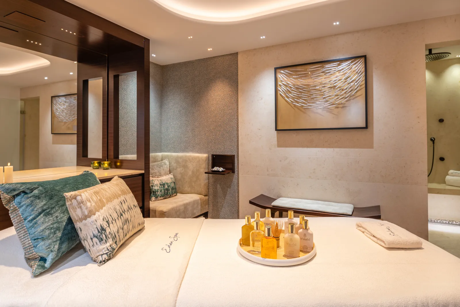 A spa treatment cabin: the bed with cushions and a tray of oils, a picture on the wall and soft light.