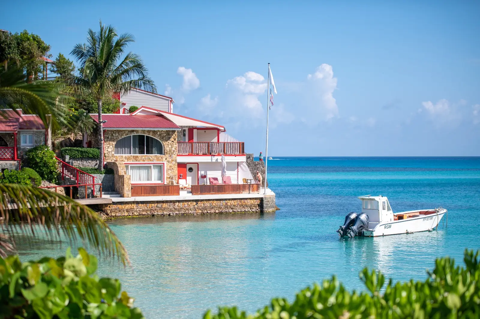 The red-roofed buildings on the rock at water level, with a small white boat moored on the turquoise sea.