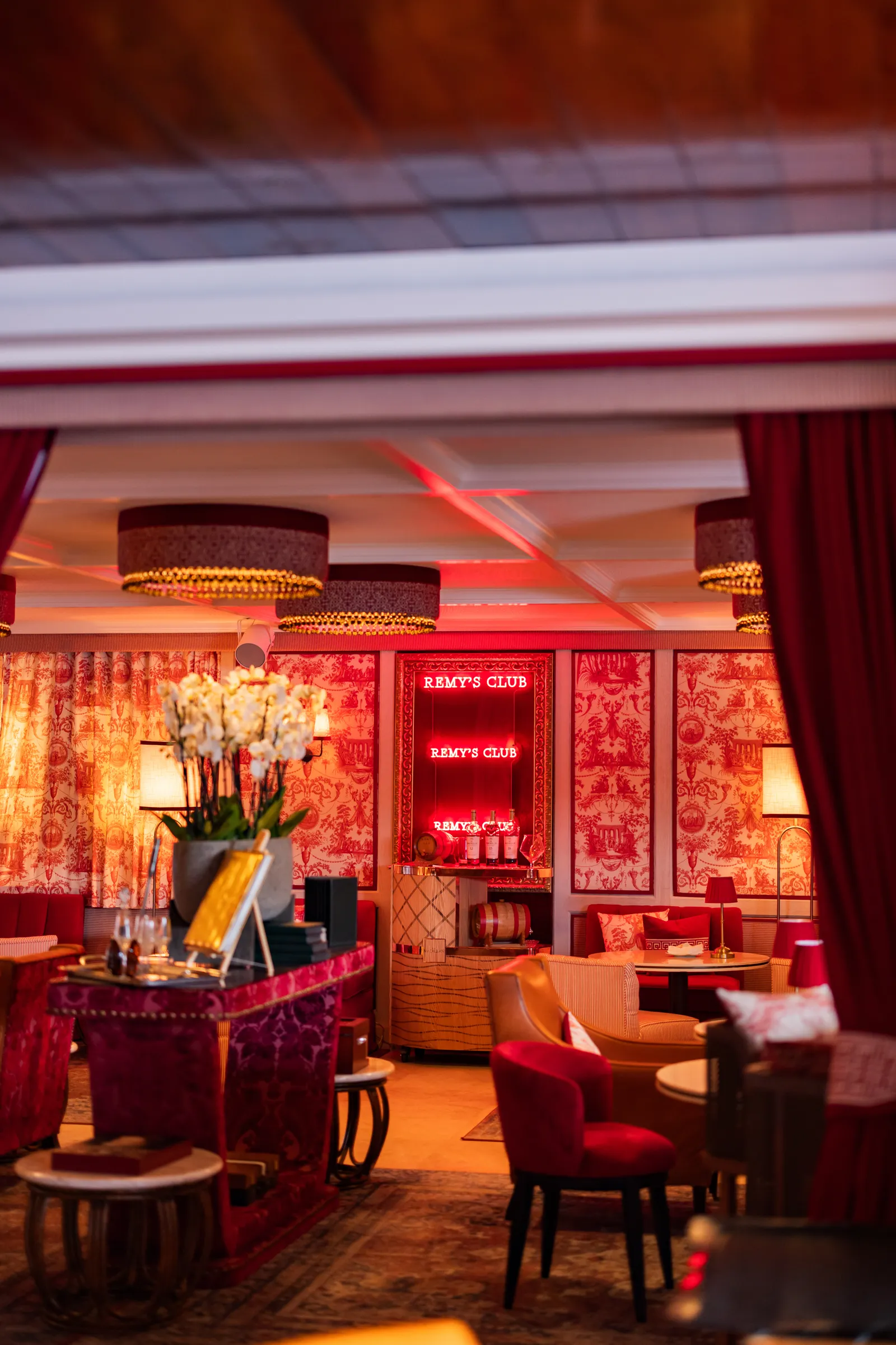 Inside the Rémy Bar: red walls and curtains, armchairs, a vase of orchids and low light.