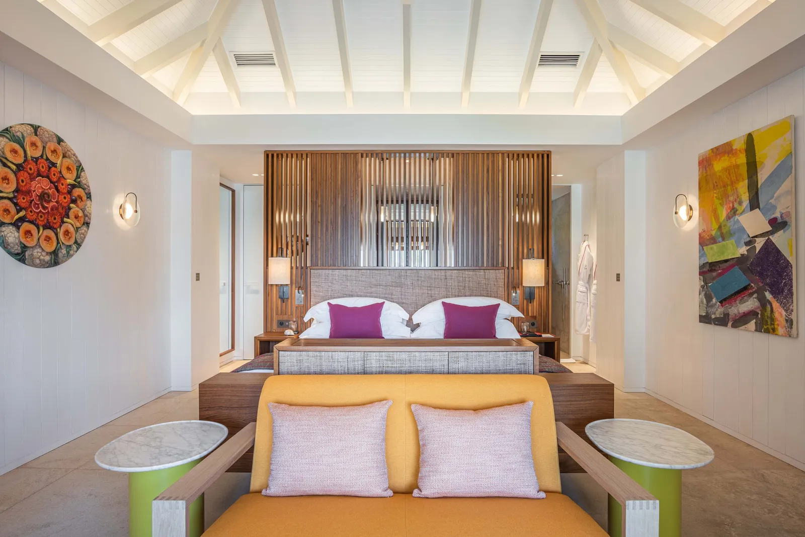 A Beach Room: the bed under a white pitched ceiling, a slatted timber headboard and a yellow sofa at the foot of the bed.