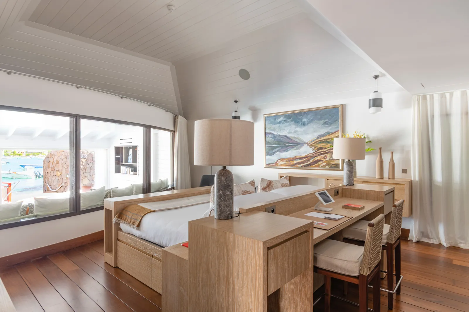 Diamond Suite James: the bed and desk in a white beamed room with a long window on the water.