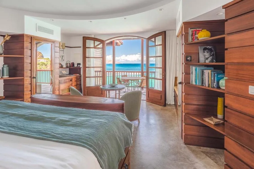 Legacy Suite Garbo: the bed with its green cover in a round room, and arched doors open to the balcony and the turquoise sea.