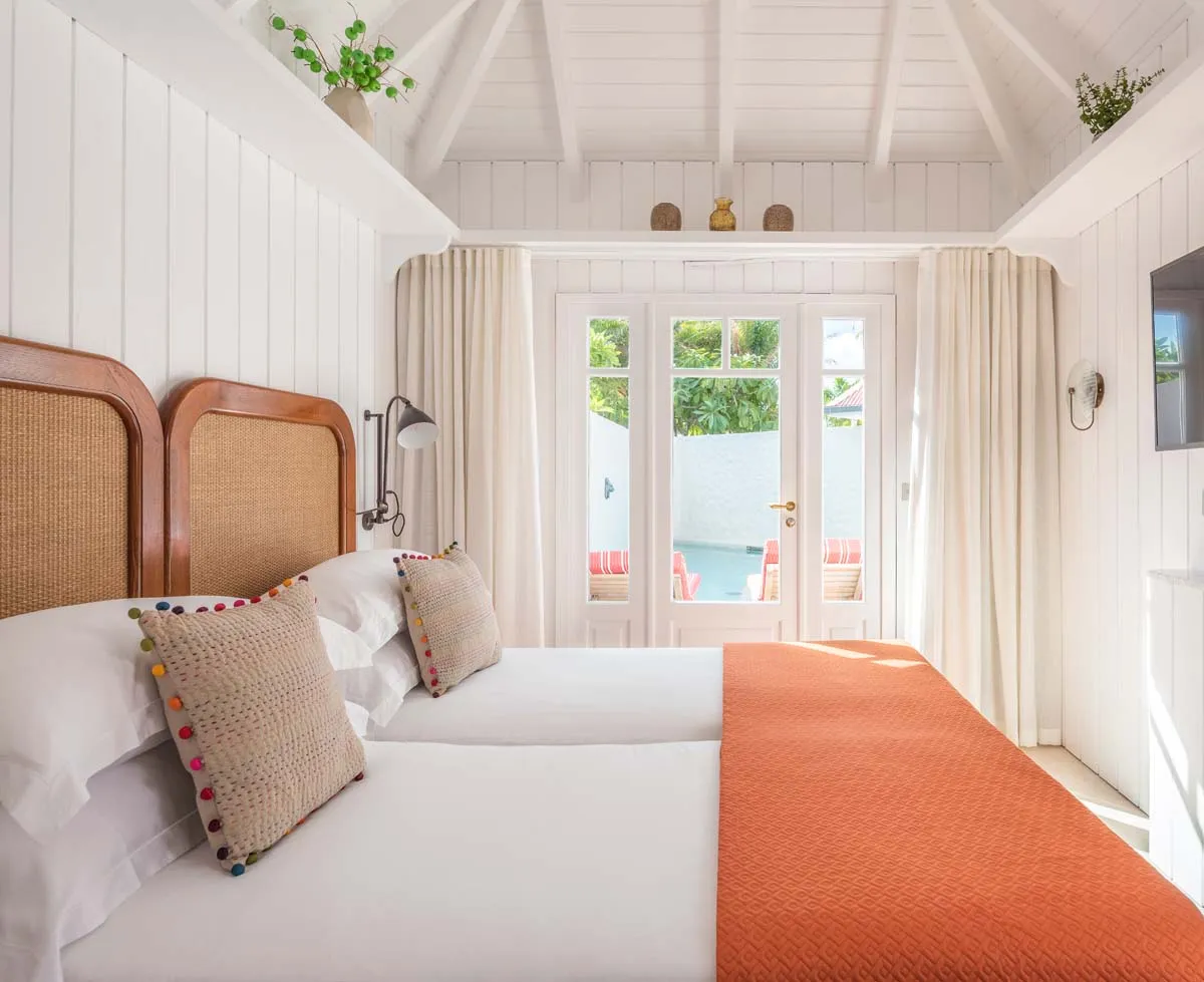 Premium Suite Fontaine: the bed with an orange throw under a white pitched ceiling, and French windows to the terrace.