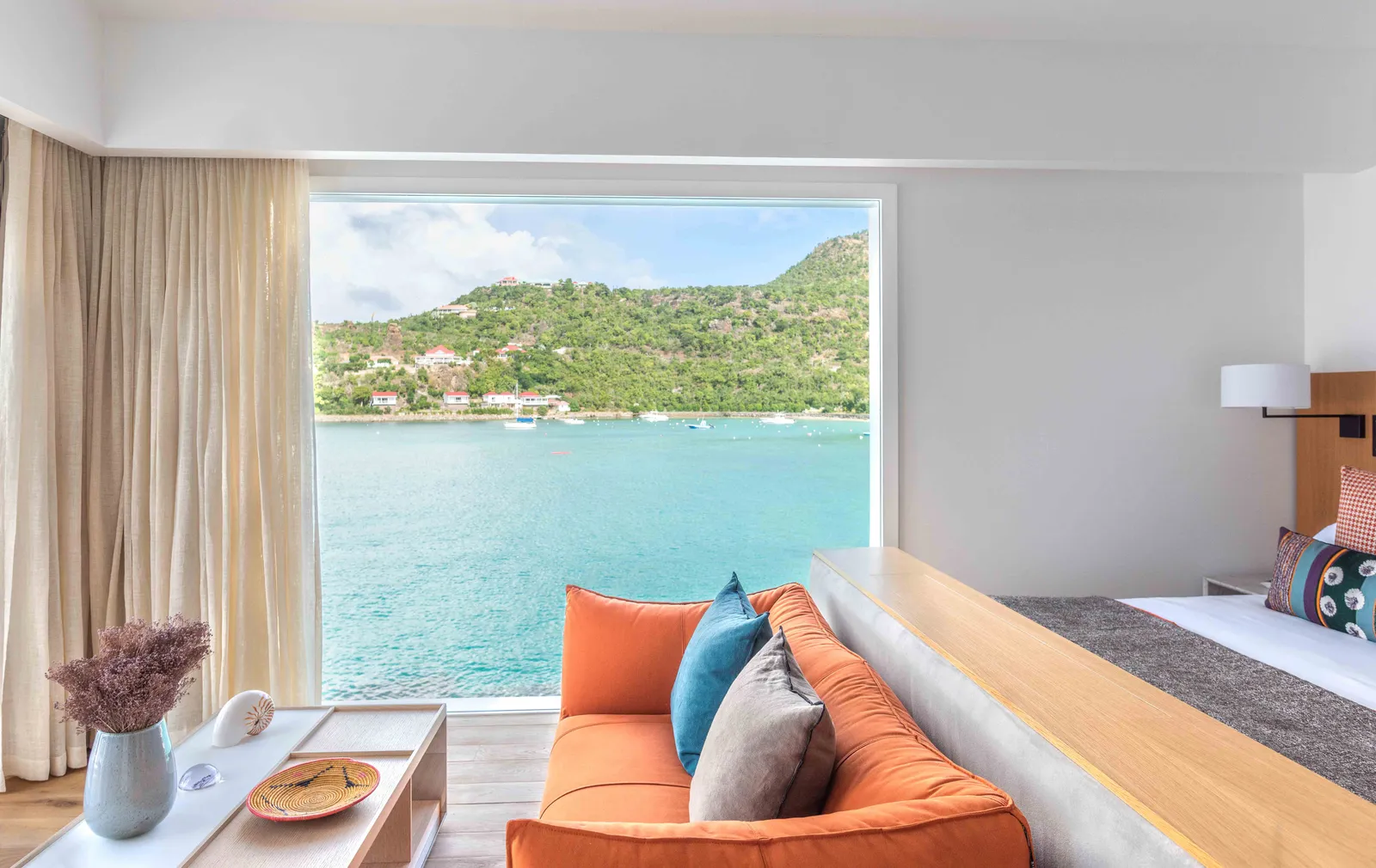 Premium Suite Fregate: an orange sofa at the foot of the bed, before the picture window on the bay and the green headland.