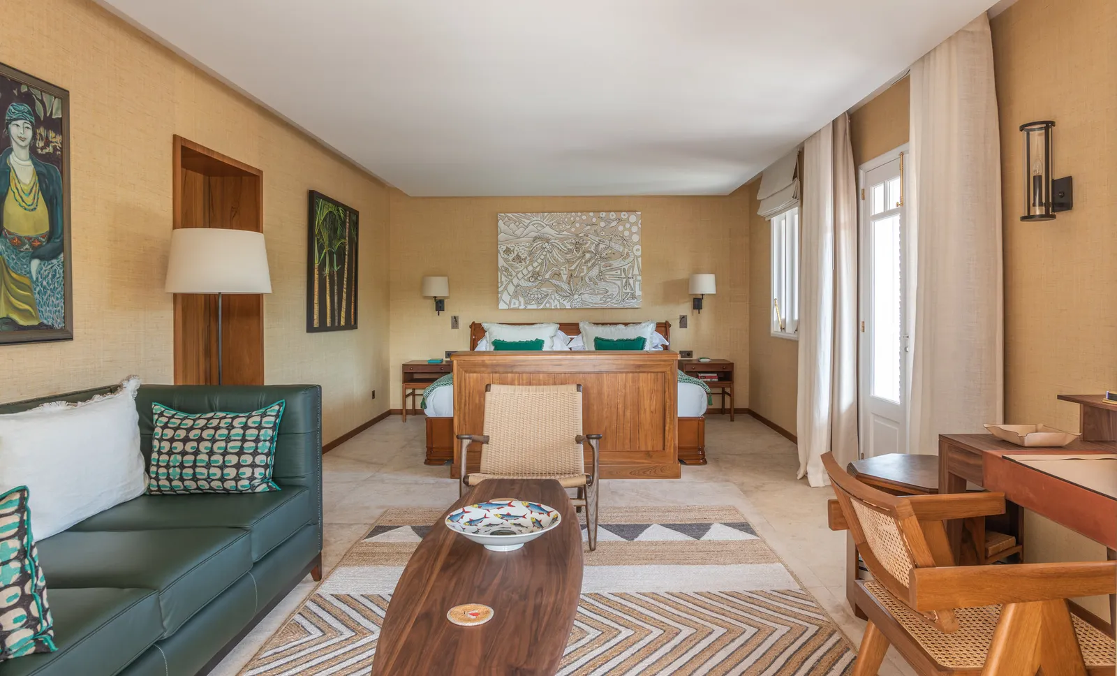 Rock Suite Flamboyant: straw-coloured walls, a dark green leather sofa, the timber-framed bed and paintings.