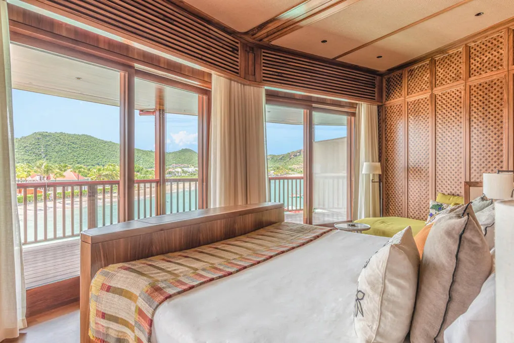 Signature Suite Jane: the bed in a timber-panelled room with windows on 3 sides above the bay and the beach.