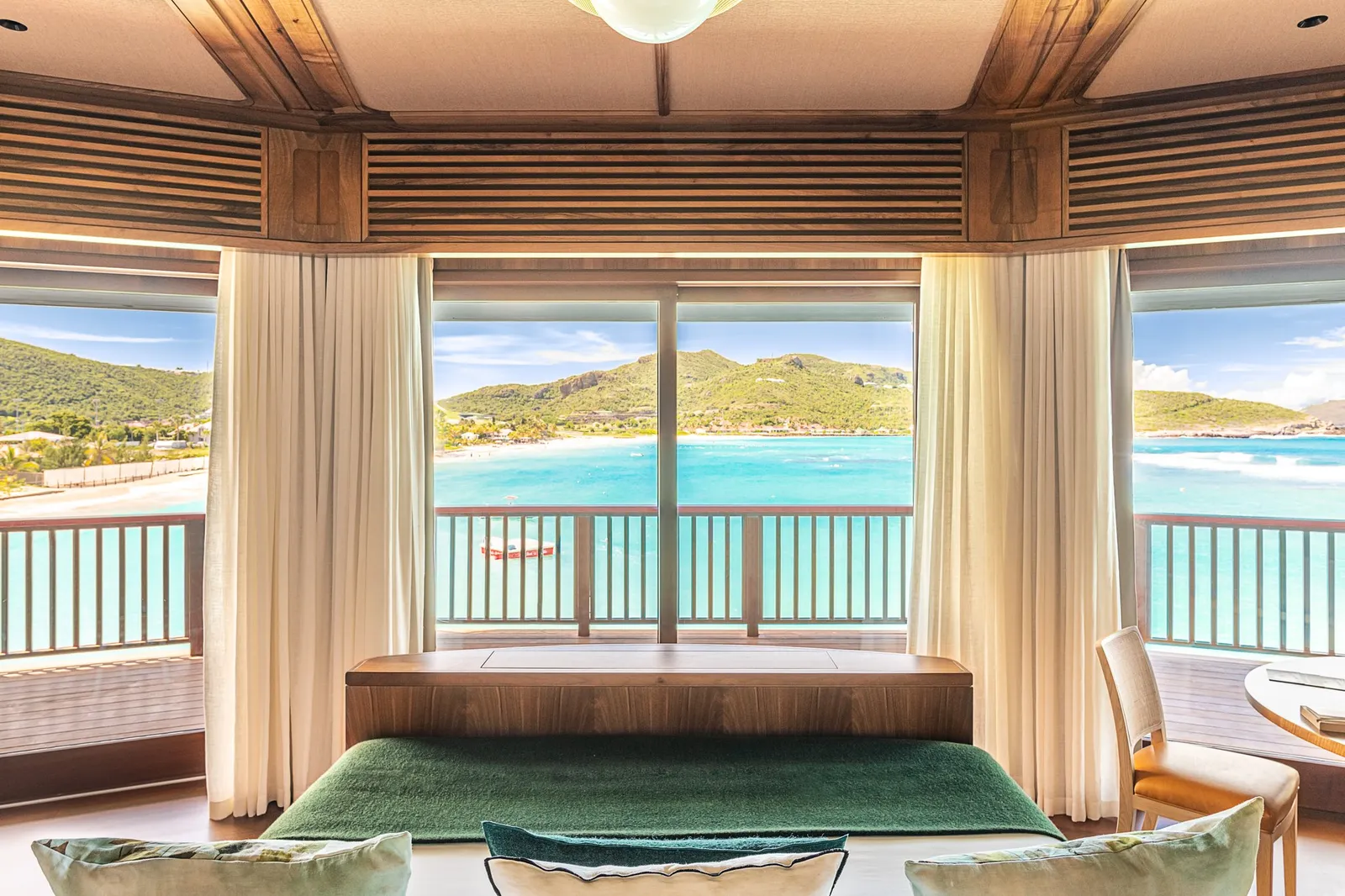 Signature Suite Pippa: the bed with its green cover facing a wall of windows on the bay, between white curtains.