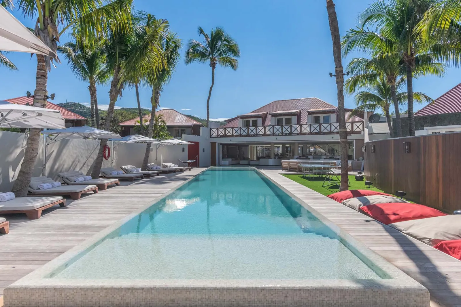 Villa Rockstar’s long pool between 2 timber decks with loungers, palms and the villa at the far end.