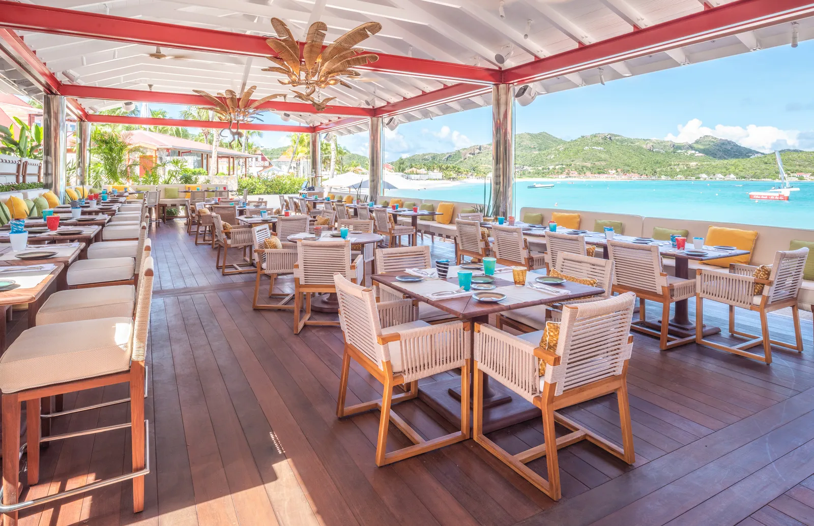 The Sand Bar’s terrace: timber tables and chairs under red-and-white striped beams, open to the bay and the hills.