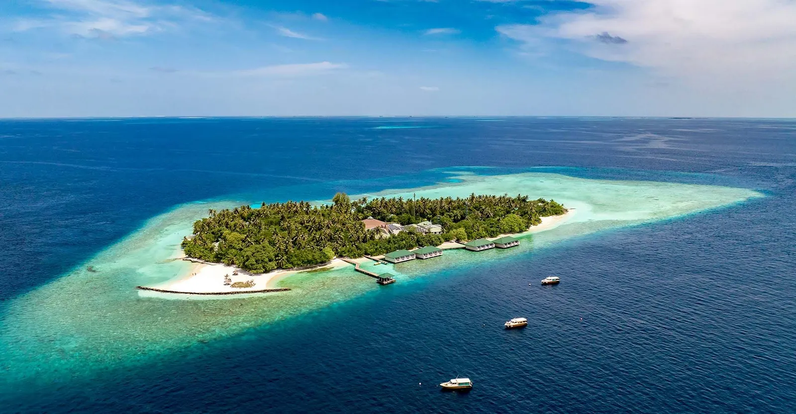 Embudu seen from afar: an oval of palms in the deep blue, the pale ring of the reef and the water villas on its right-hand side.