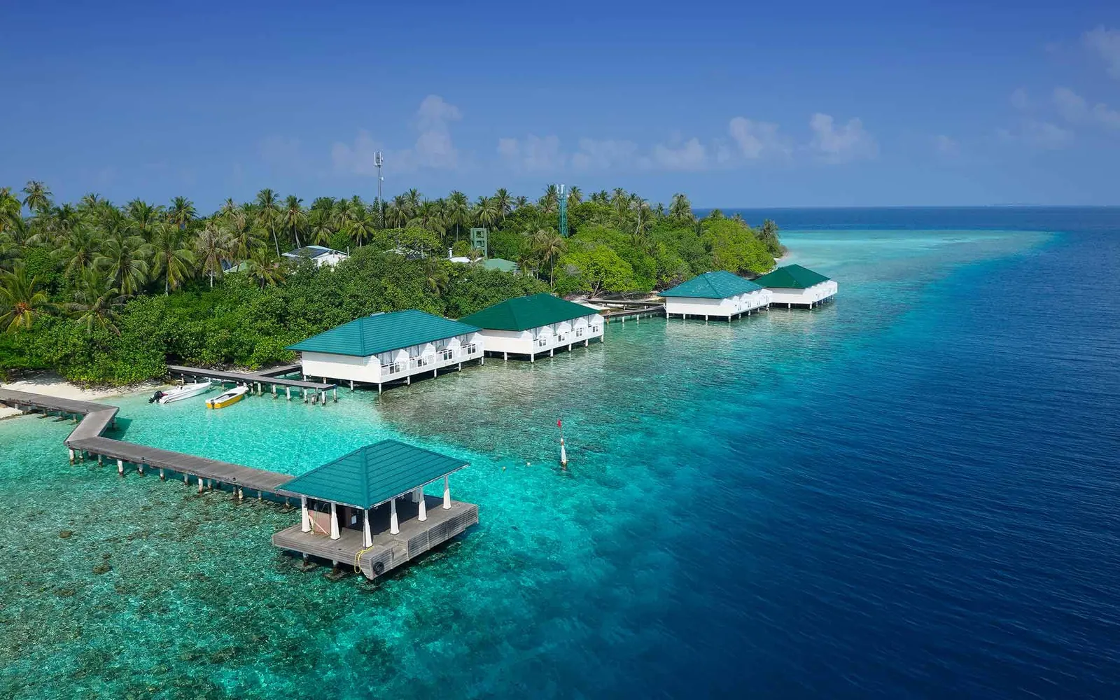 The water villas from above: their green roofs in a row over the lagoon, the timber walkway and the green island behind.