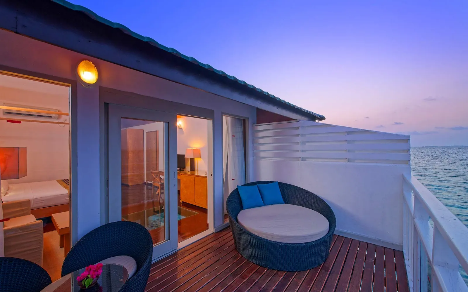 A water villa’s balcony at sunset, with its round lounger and the sea beyond the rail.