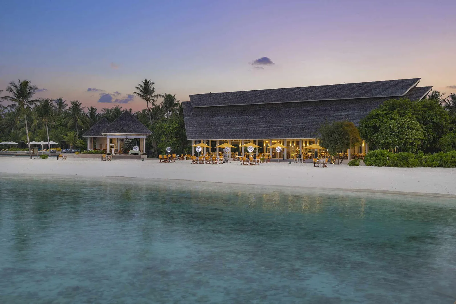 Aqua, the main restaurant, on the beach at dusk, its lights on and the lagoon calm in front.