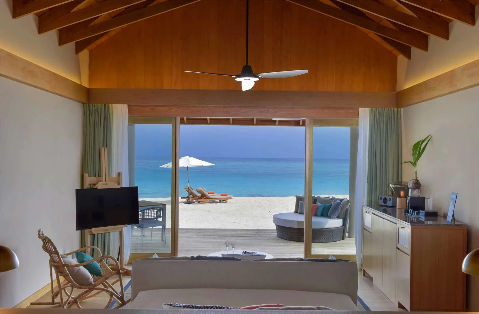 Inside a Beach Villa: the sofa, the timber ceiling and the glass doors open onto the deck with its daybed, the beach and the sea.