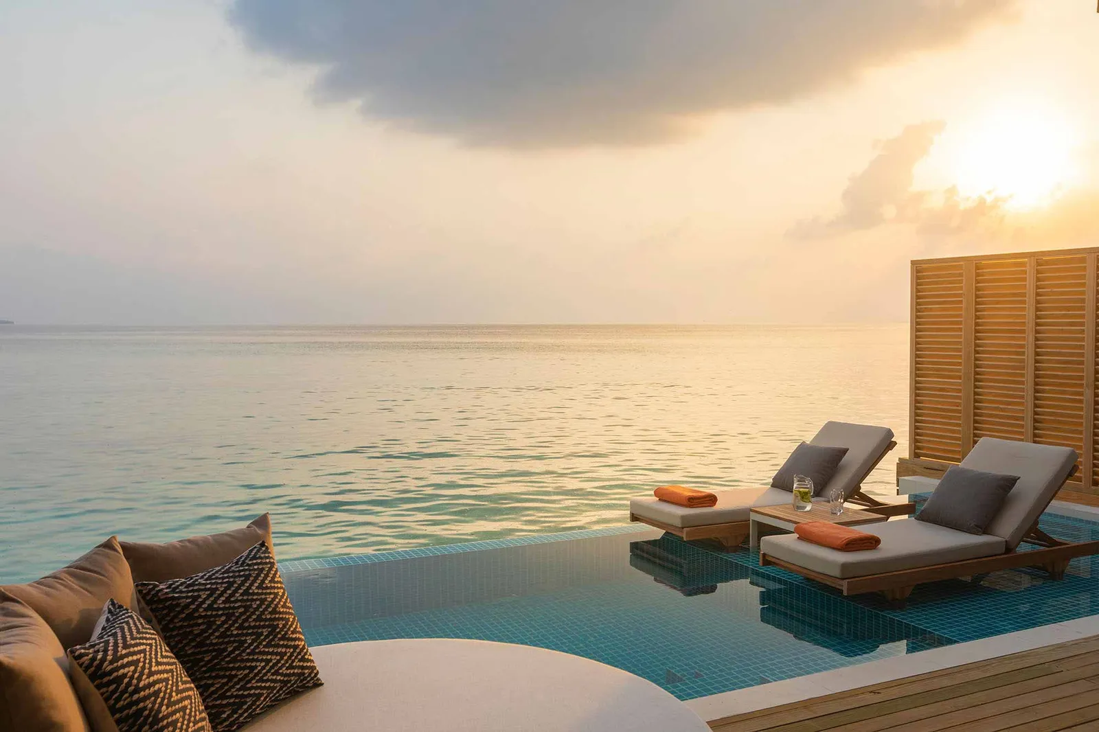 The infinity pool on a Sunset Water Villa’s deck, with 2 loungers and the sun low over the sea.