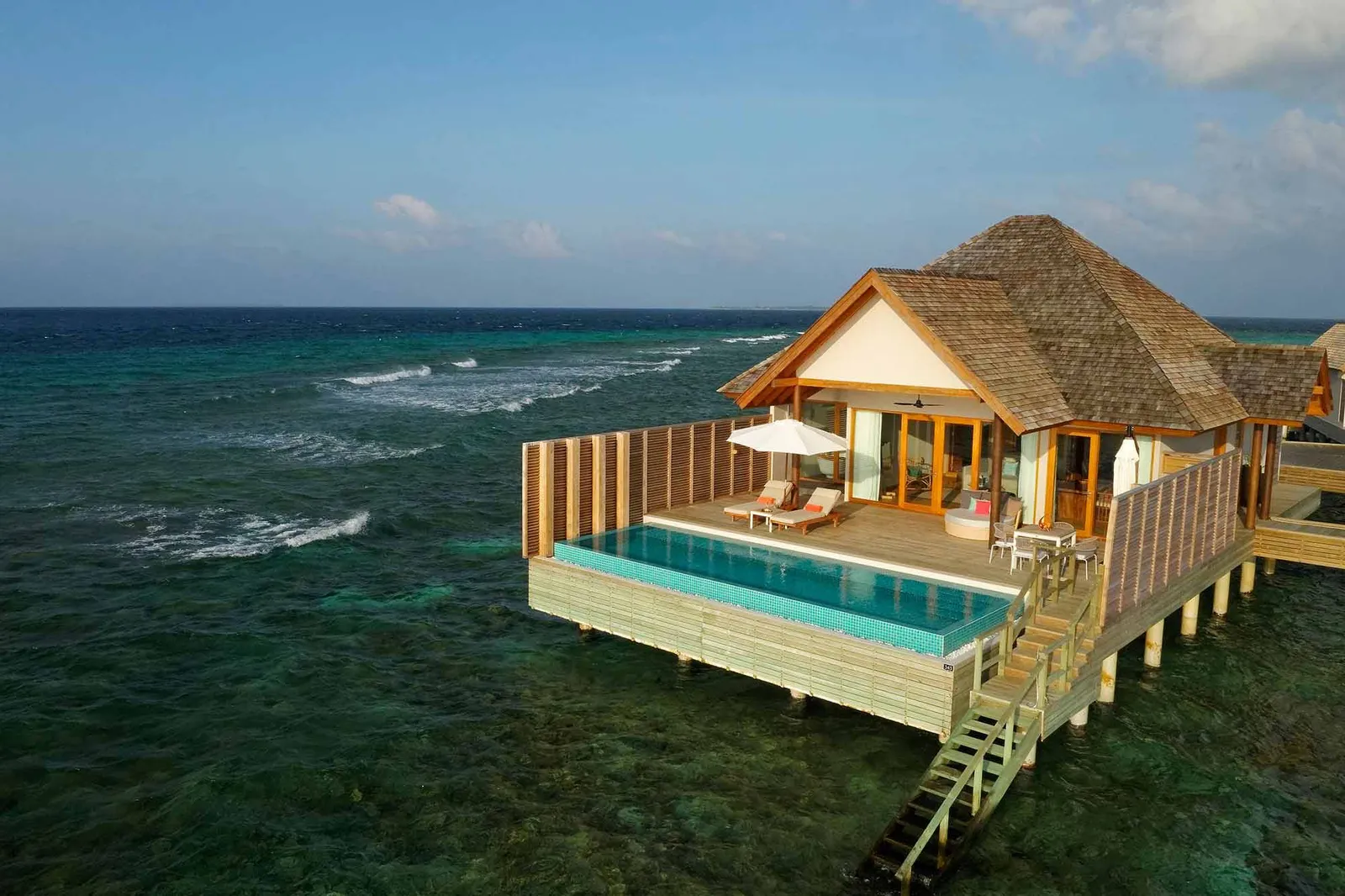 A Superior Water Villa from above at the tip of the jetty: the thatched roof, the pool on the deck and the steps into the sea.