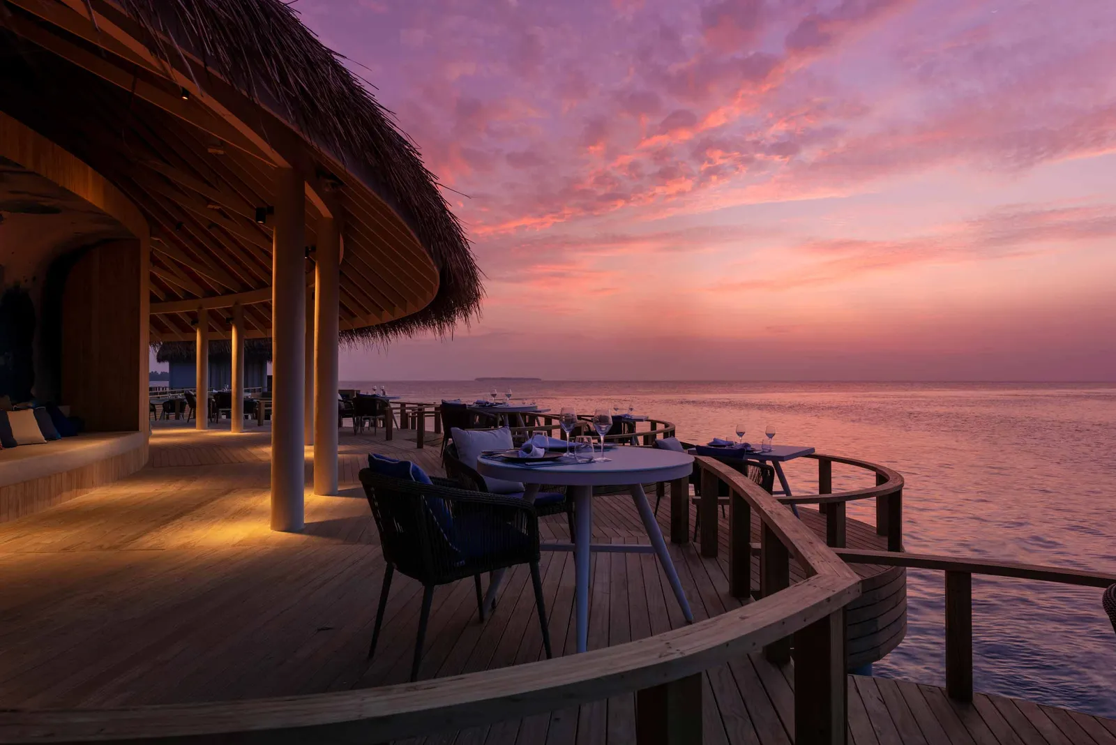 Mediterraneo’s terrace over the water at dusk, tables laid under the thatched roof and a pink sky.