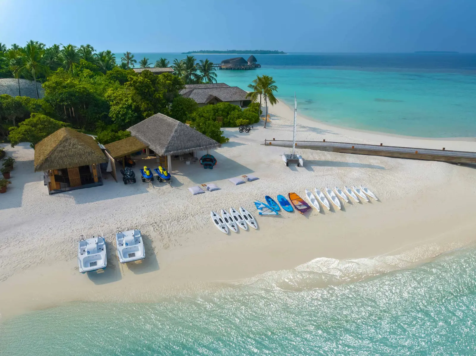 The water sports centre from above: kayaks, boards and pedalos lined up on the beach beside a thatched hut.