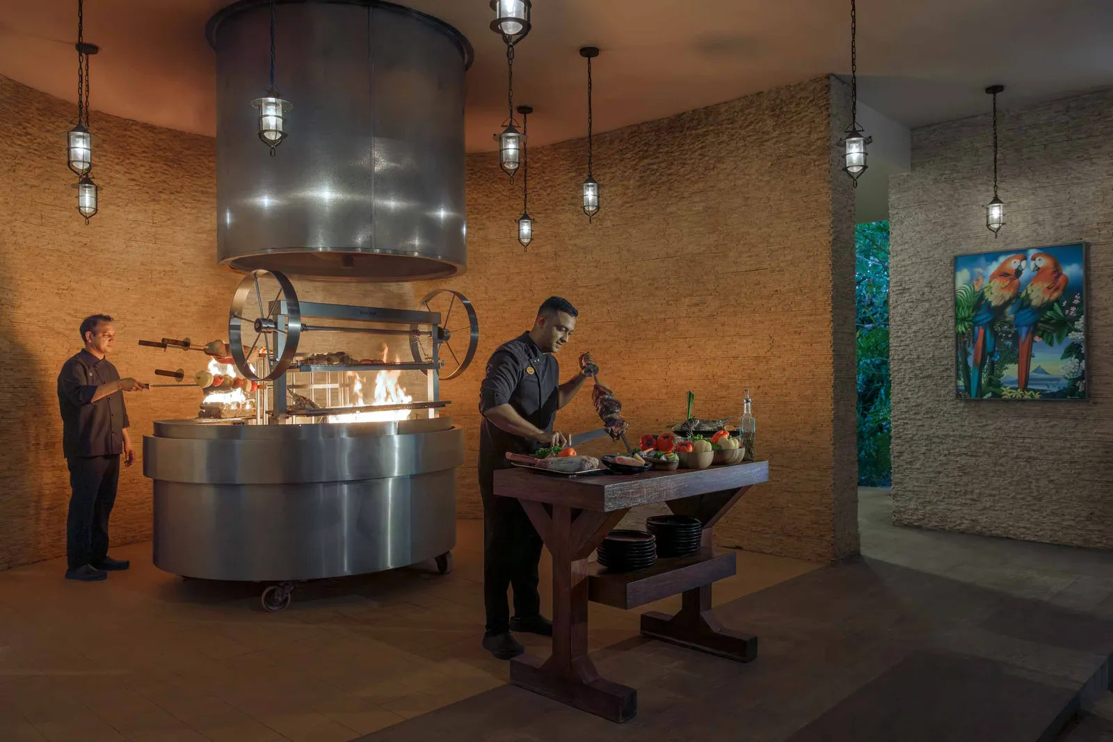 The grill at Amazònico: 2 cooks at the coals under the hood, with skewers of meat.