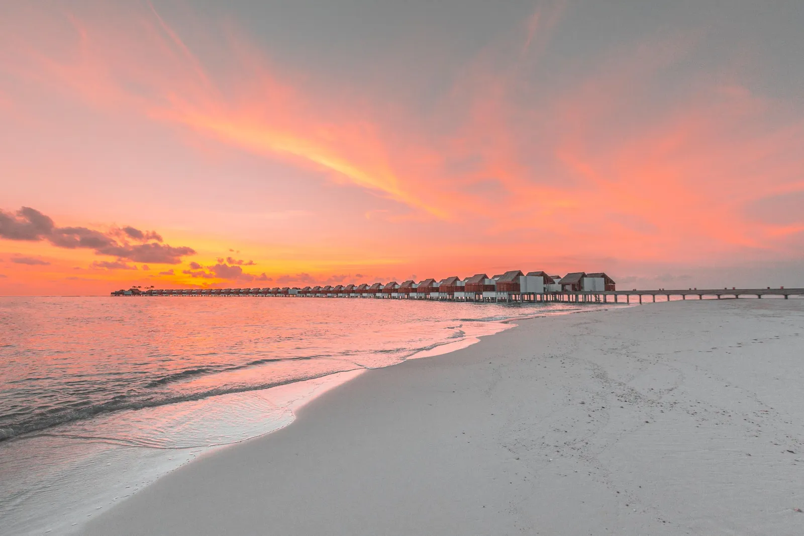 The beach at sunset, the sky pink and orange and the line of water villas on the horizon.