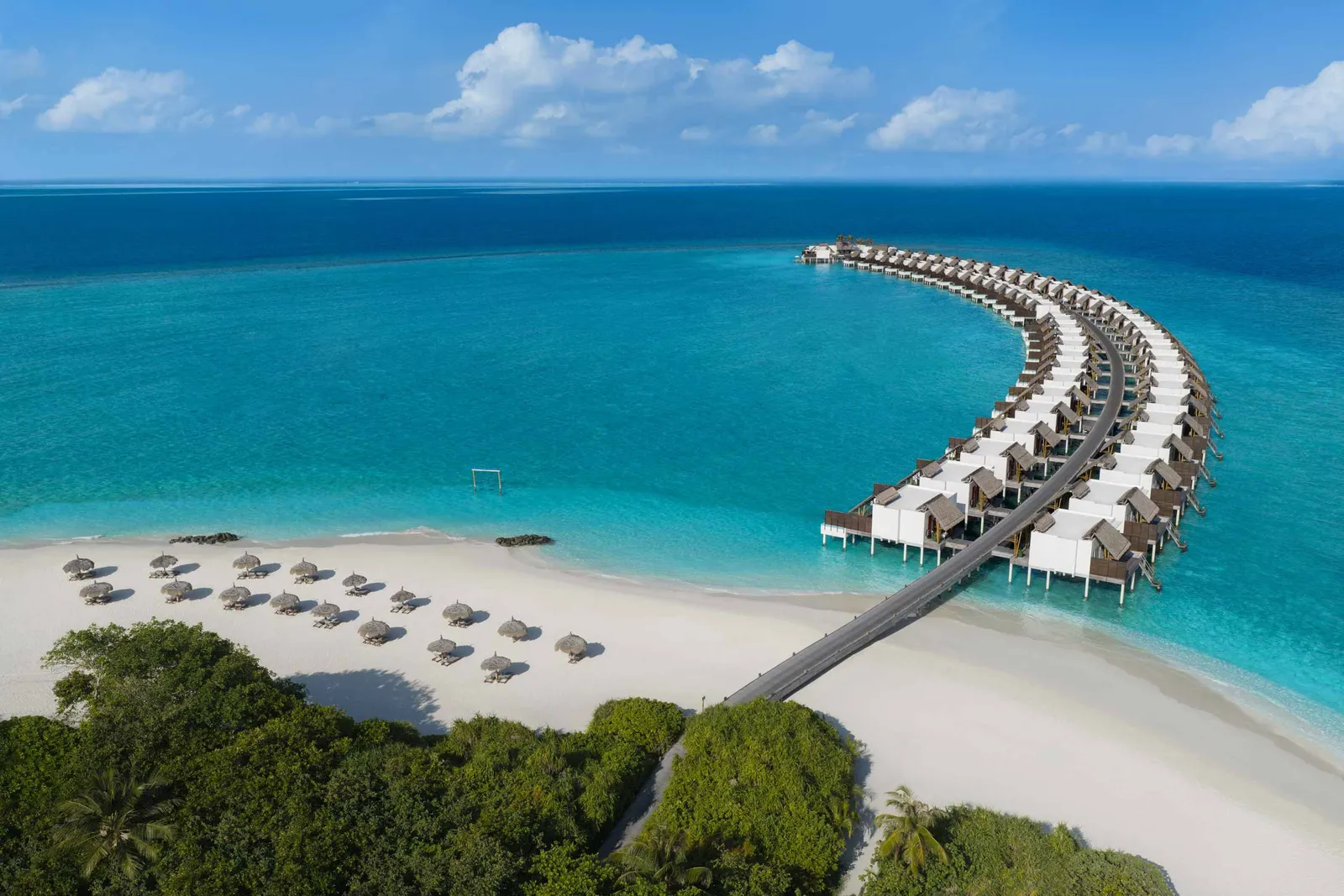 The crescent of water villas running out from the beach, thatched parasols on the sand and the open sea beyond.