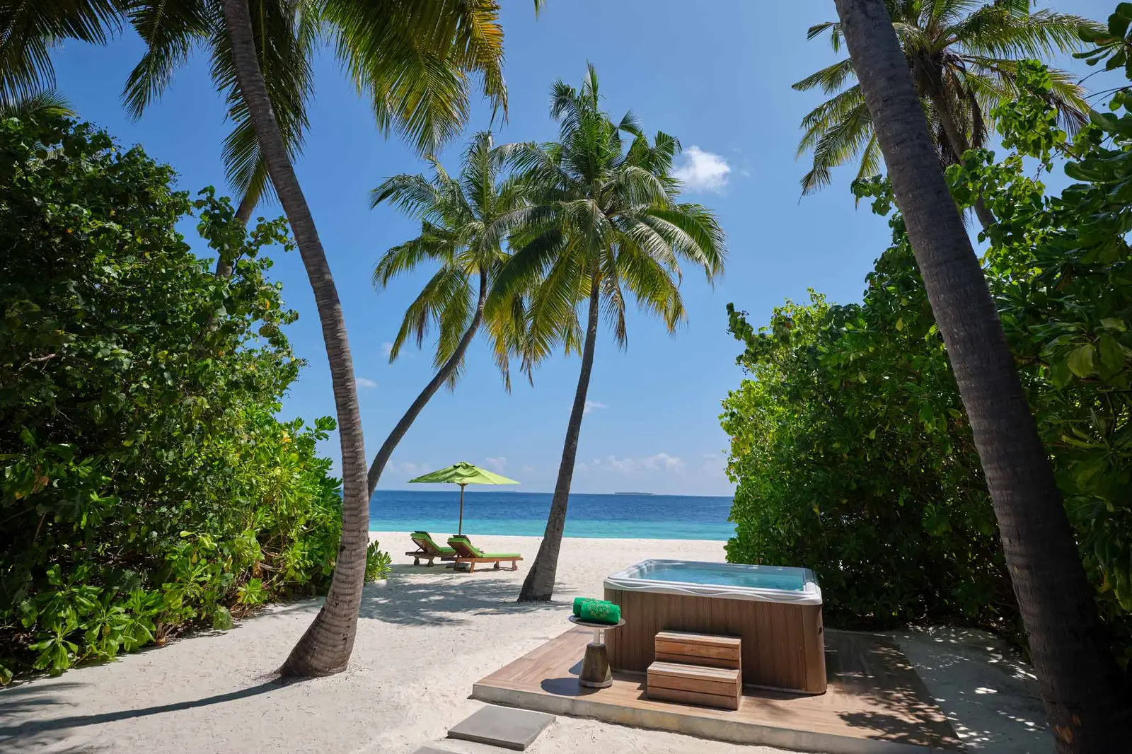 A Jacuzzi Beach Villa’s hot tub on the sand among the palms, the beach and the sea ahead.