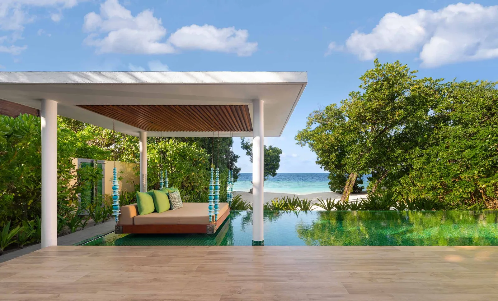 The pavilion with its hanging daybed over a Superior Beach Villa’s infinity pool, the sea beyond the trees.