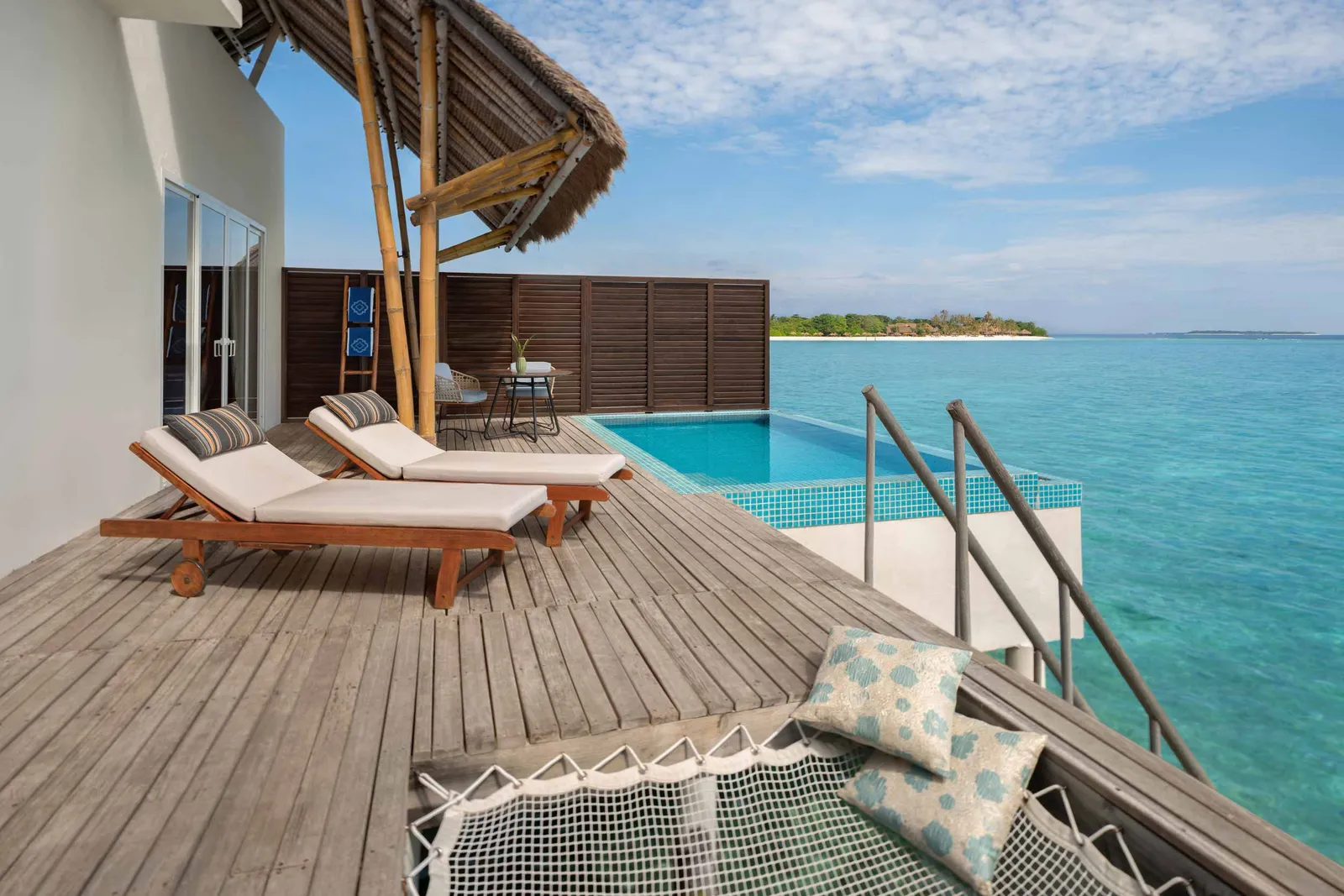 A Water Villa with Pool’s deck, with its loungers, the hanging net and the infinity pool over the sea.