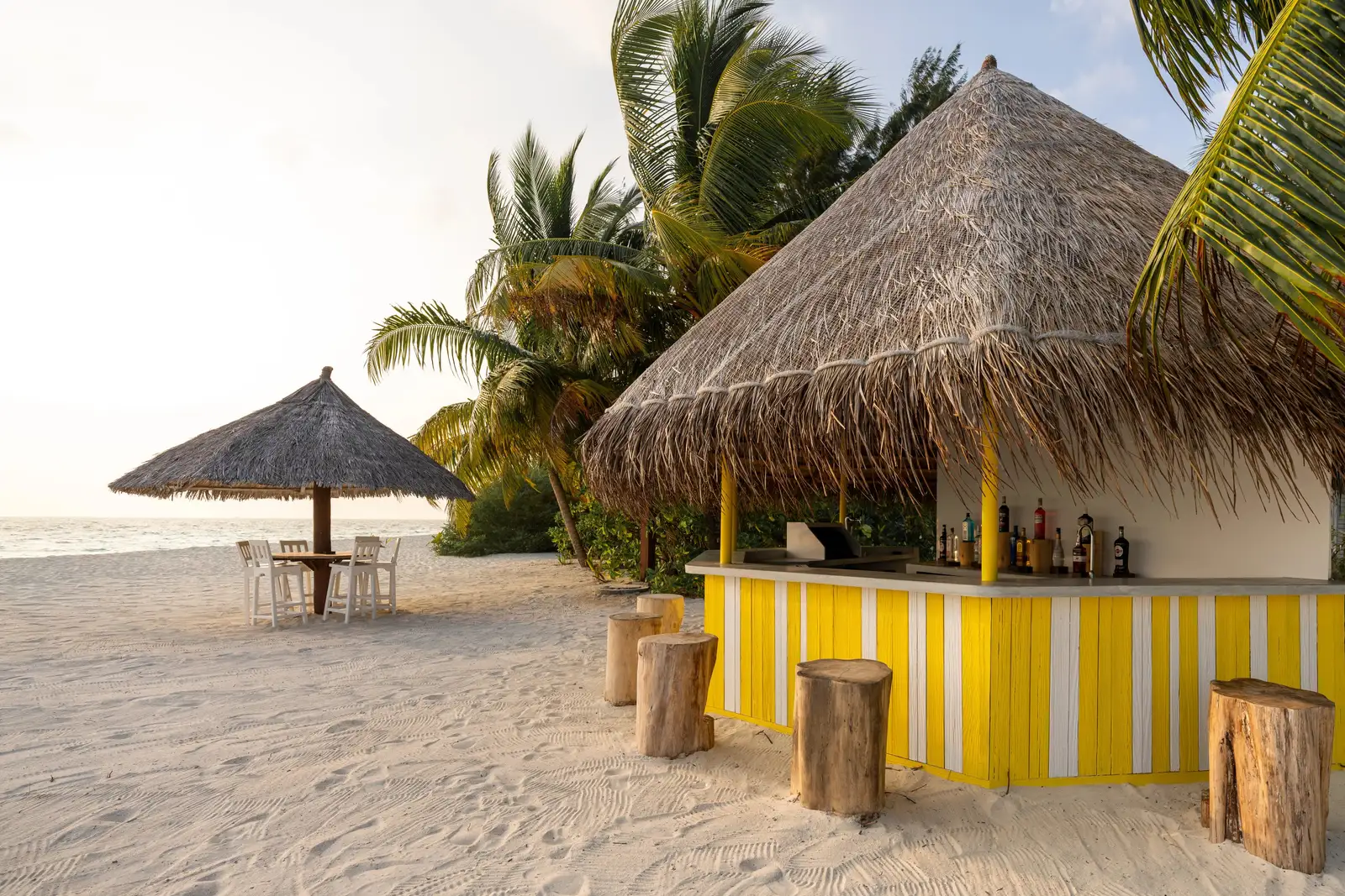The Beach Shack on the sand: its yellow-and-white striped bar under a thatched roof and its palm-trunk stools.