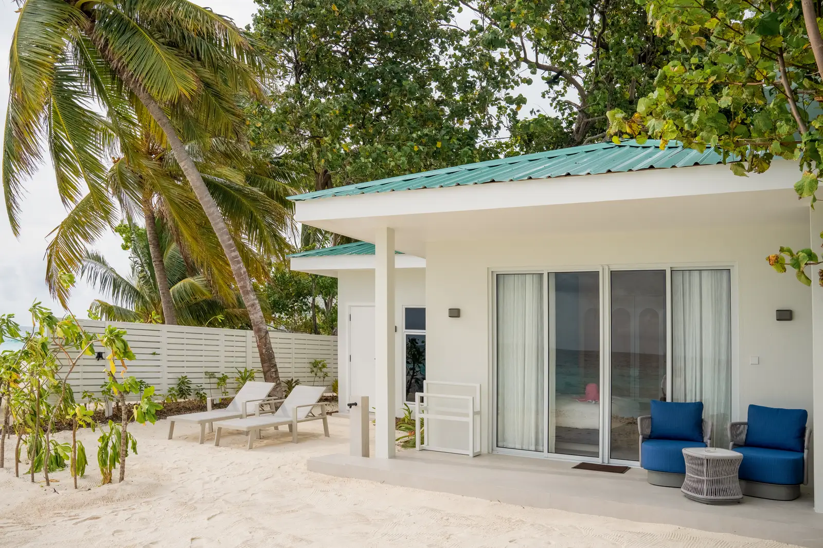The Beach Suite on the sand among the palms: the white pavilion, its terrace with blue armchairs and its glass doors.