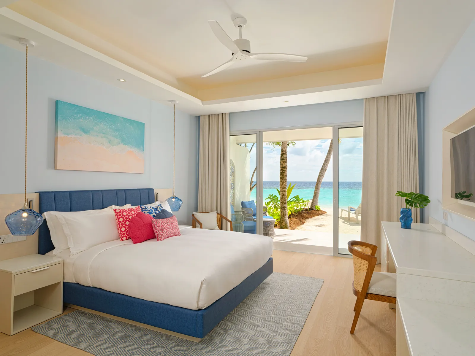A Beach Villa bedroom, with the king bed, a desk and the glass doors onto the terrace and the sea.