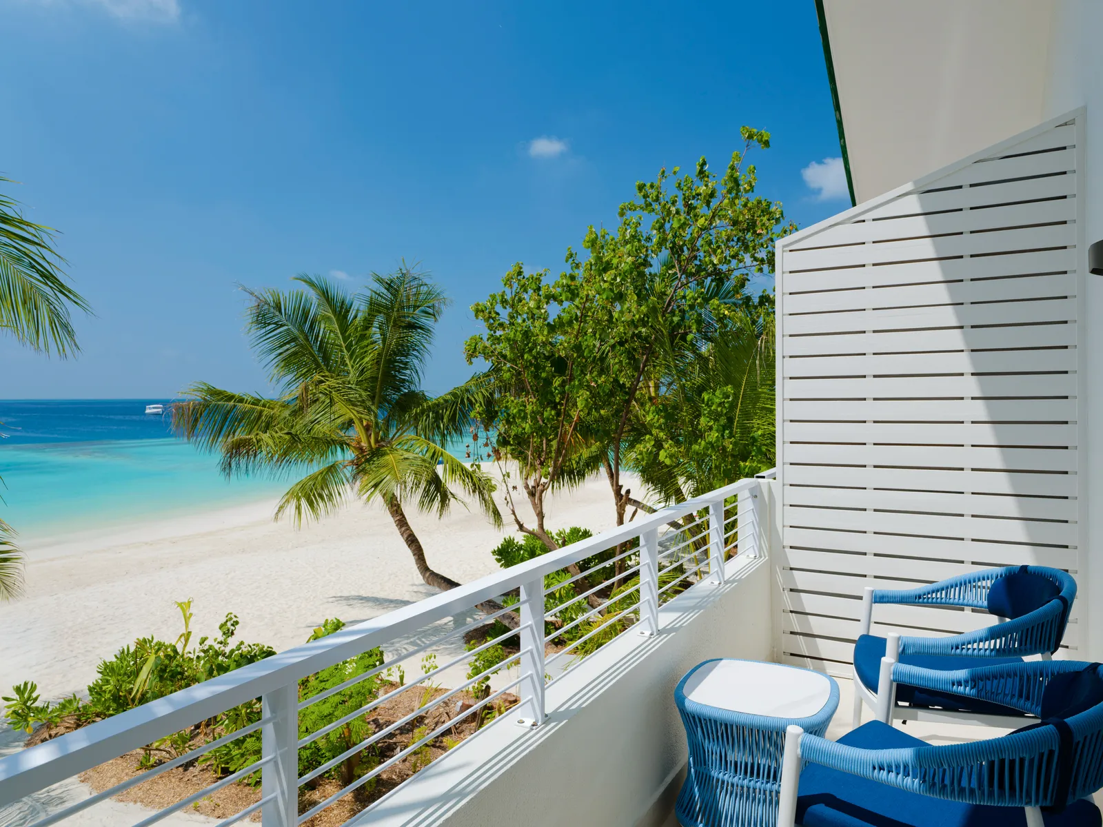 A Sky Studio balcony, with blue armchairs, a white railing and the beach among the palms below.