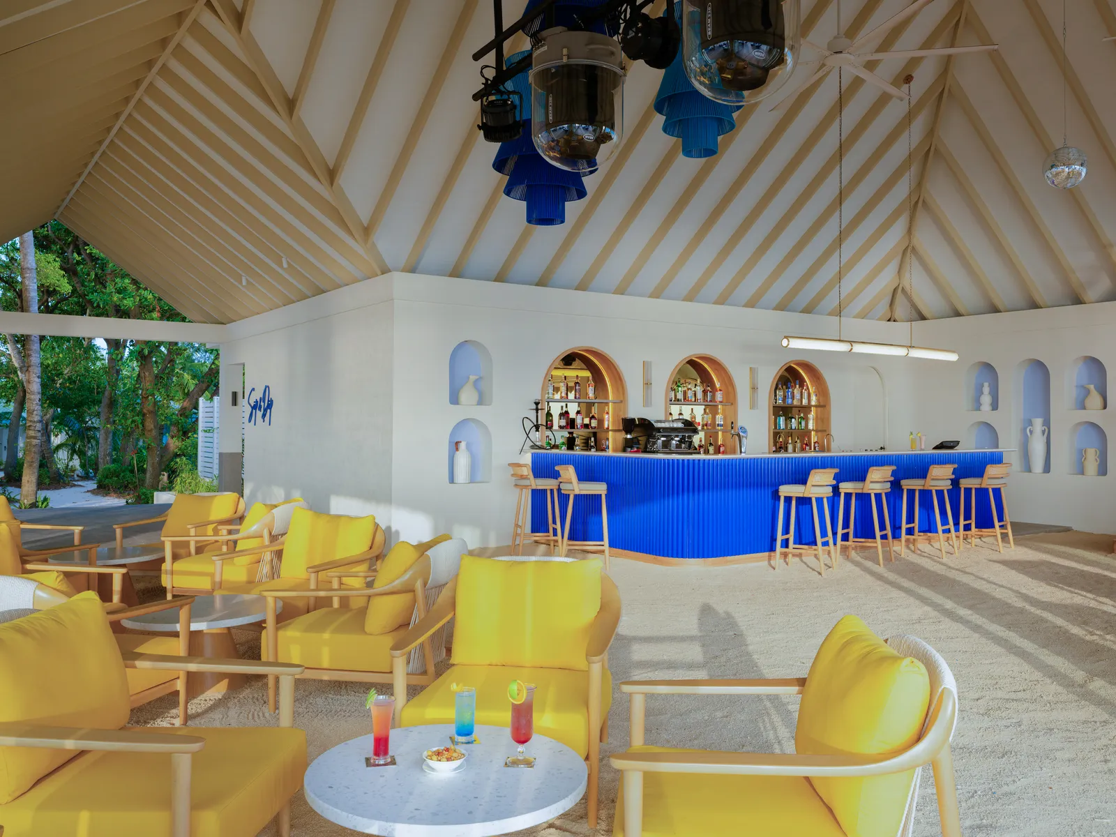 Inside Sip & Dip, with its sand floor, yellow armchairs, blue bar counter and high thatched roof.