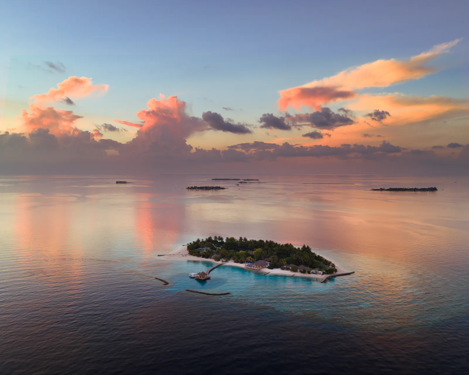 The island at dusk, small on a calm sea, with pink clouds reflected in the water.