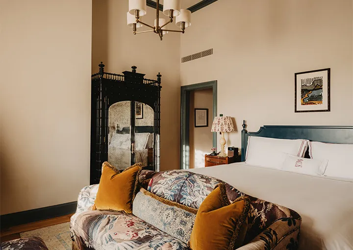 A Stable Room: a floral sofa with ochre velvet cushions at the foot of the bed