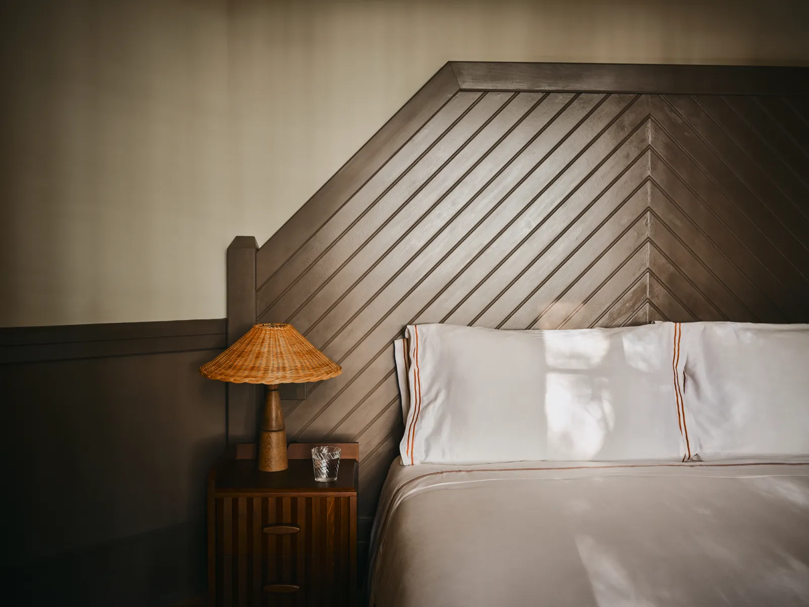 A Woodland Cabin bedroom: a chevron timber headboard and a wicker lamp