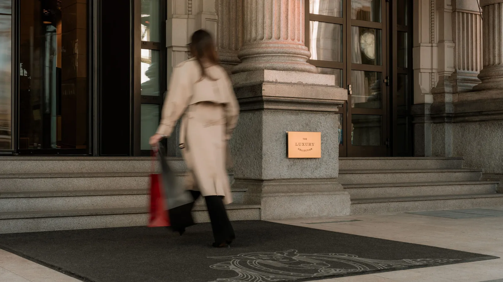 A guest walks into the hotel between the entrance columns, carrying shopping bags