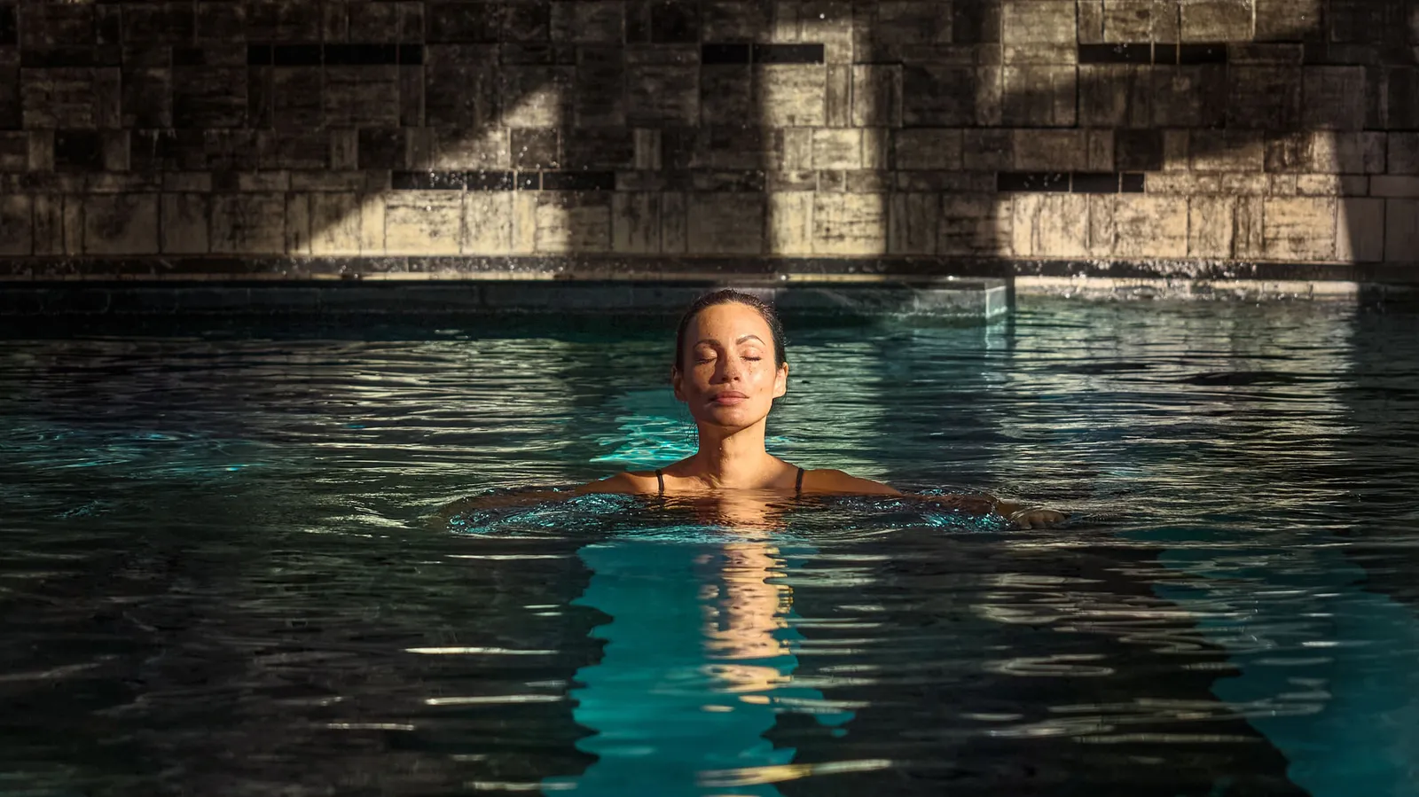 A woman swimming in the covered pool in front of the stone wall