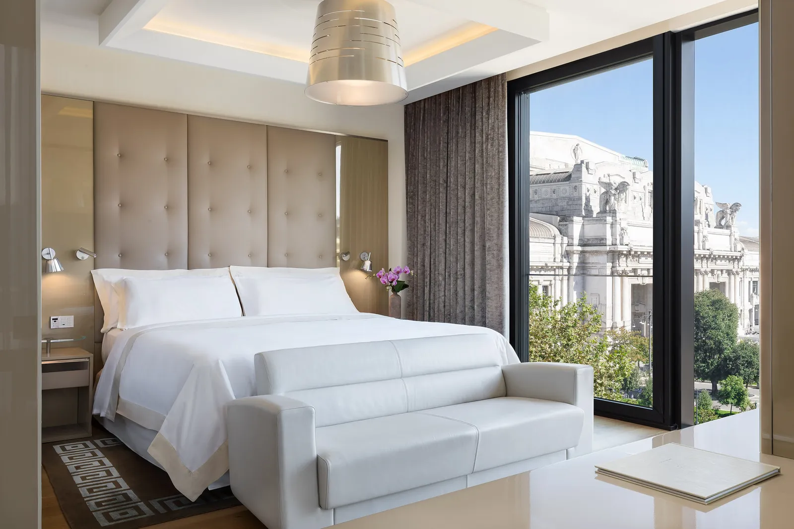 A Panoramic Suite, with the bed, a white sofa and the glass wall on Milano Centrale