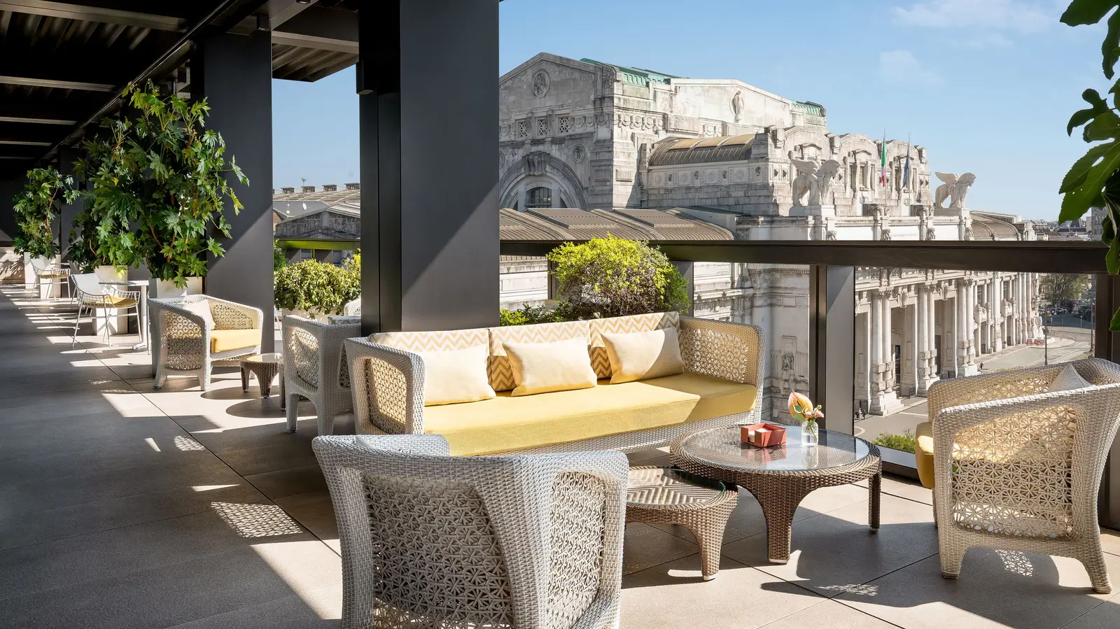 Terrazza Gallia’s terrace by day, sofas and armchairs under the pergola and the facade of Milano Centrale beyond the parapet