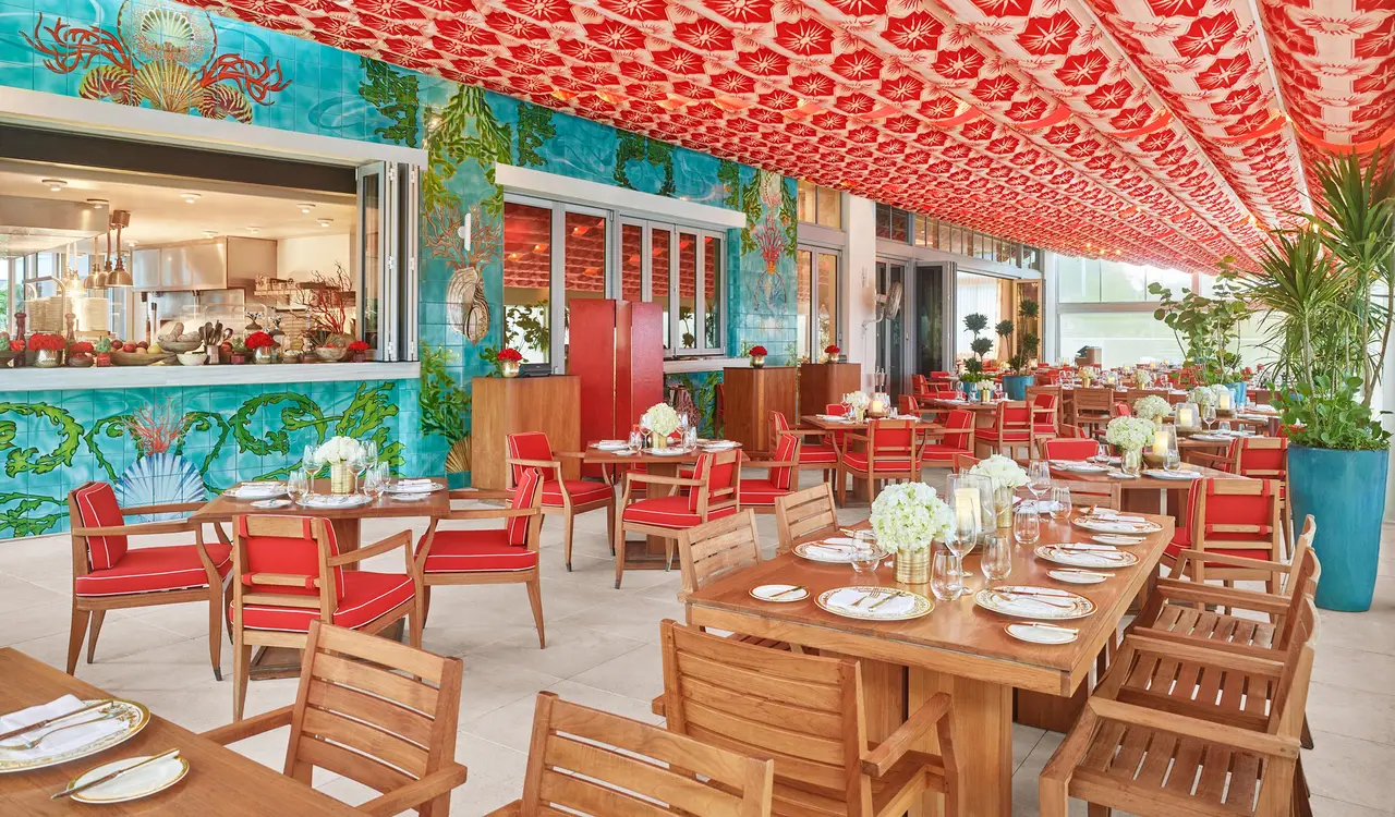 The Los Fuegos veranda: wooden tables and red chairs under a red-patterned ceiling, with a turquoise painted wall.