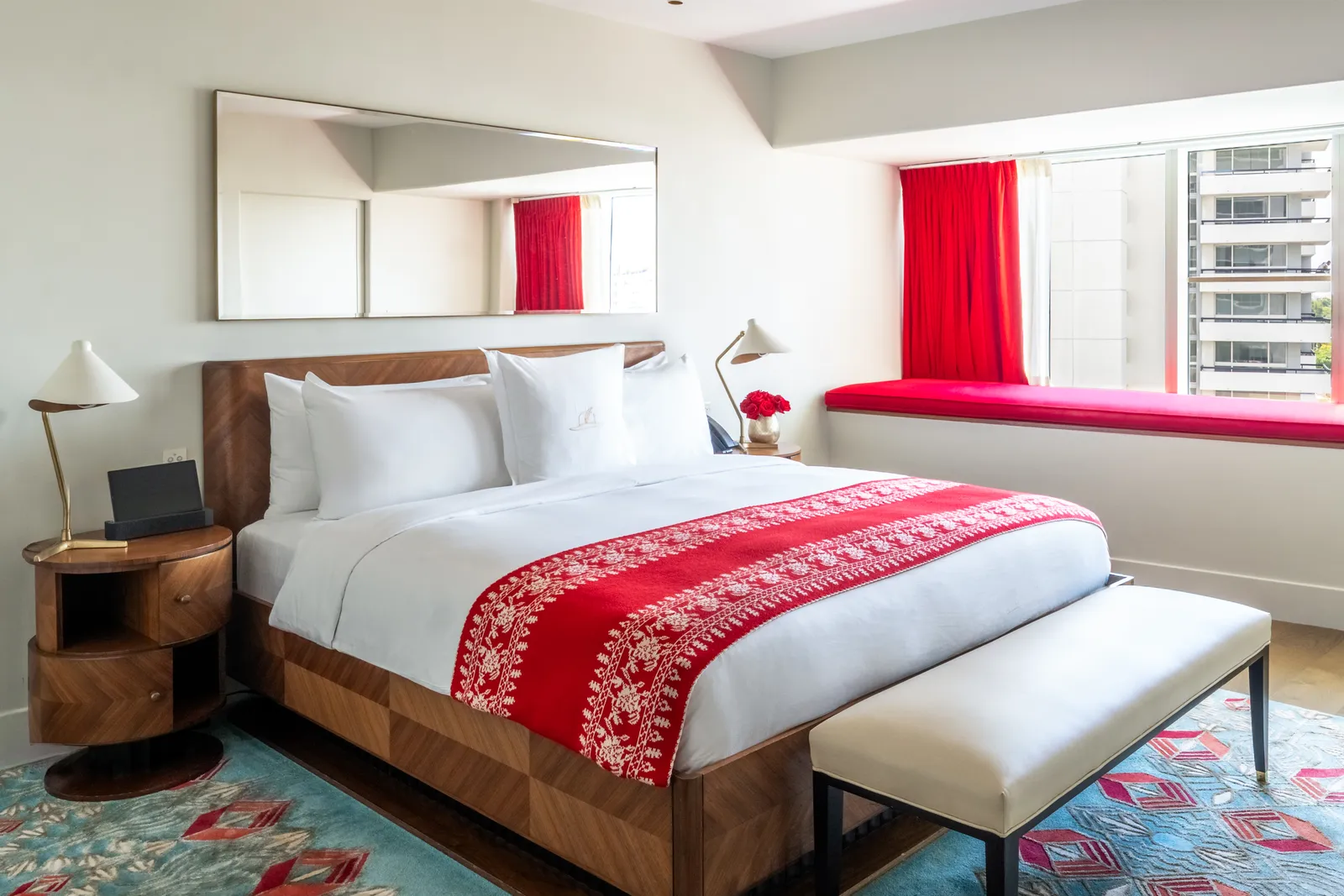 A Bay View Room: the king bed with its embroidered red runner, a pale bench at its foot and the red window seat.