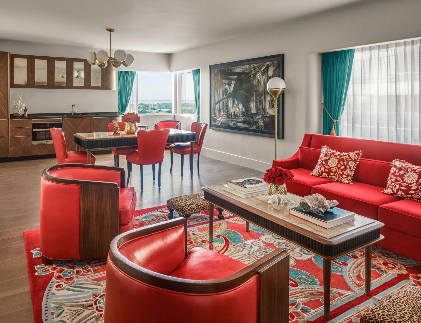 The Bay View Suite’s living room: red sofa and armchairs, the dining table and turquoise curtains.
