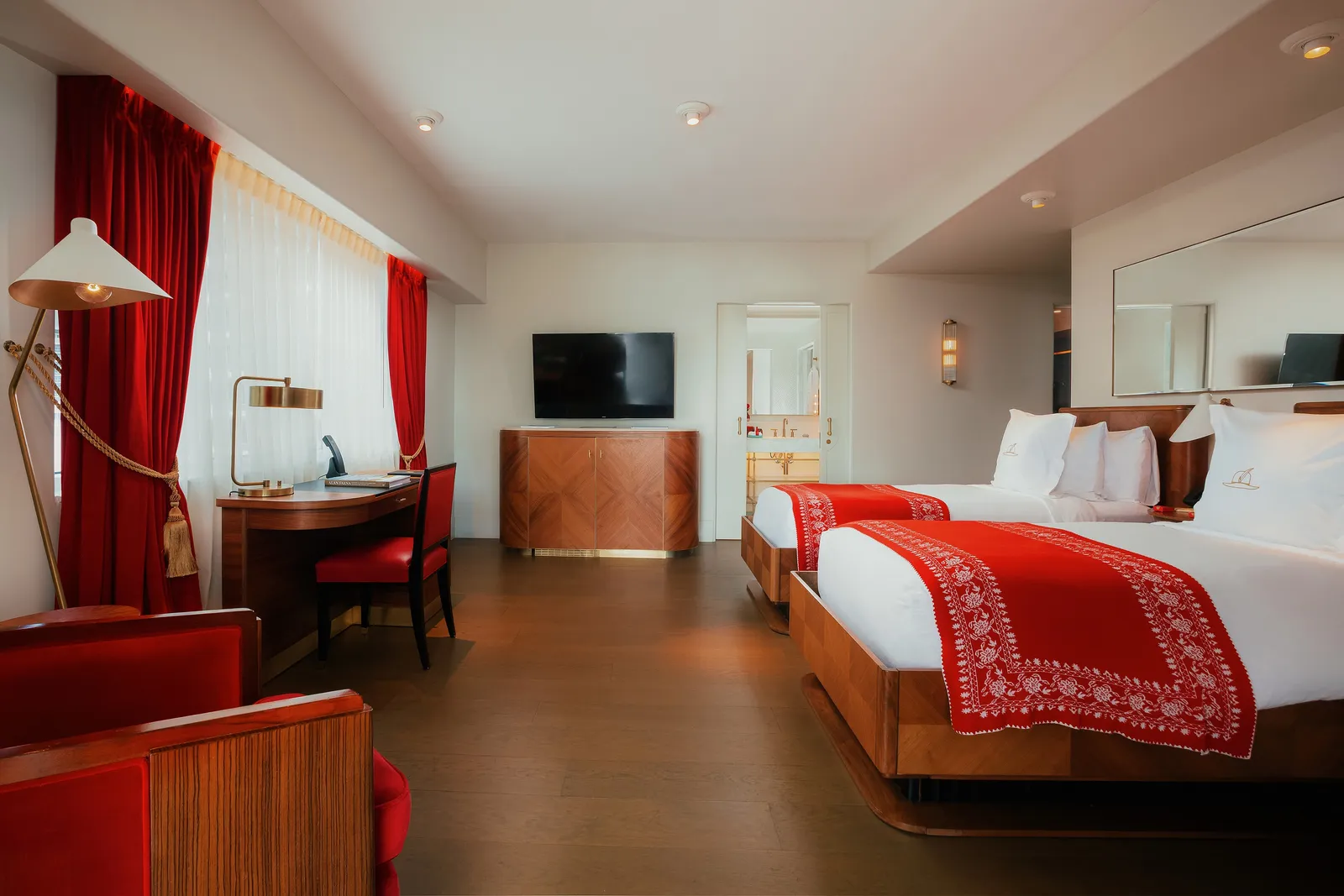 The Bay View Twin/Twin Room: 2 beds with red runners, the desk, red curtains and the window onto the city.