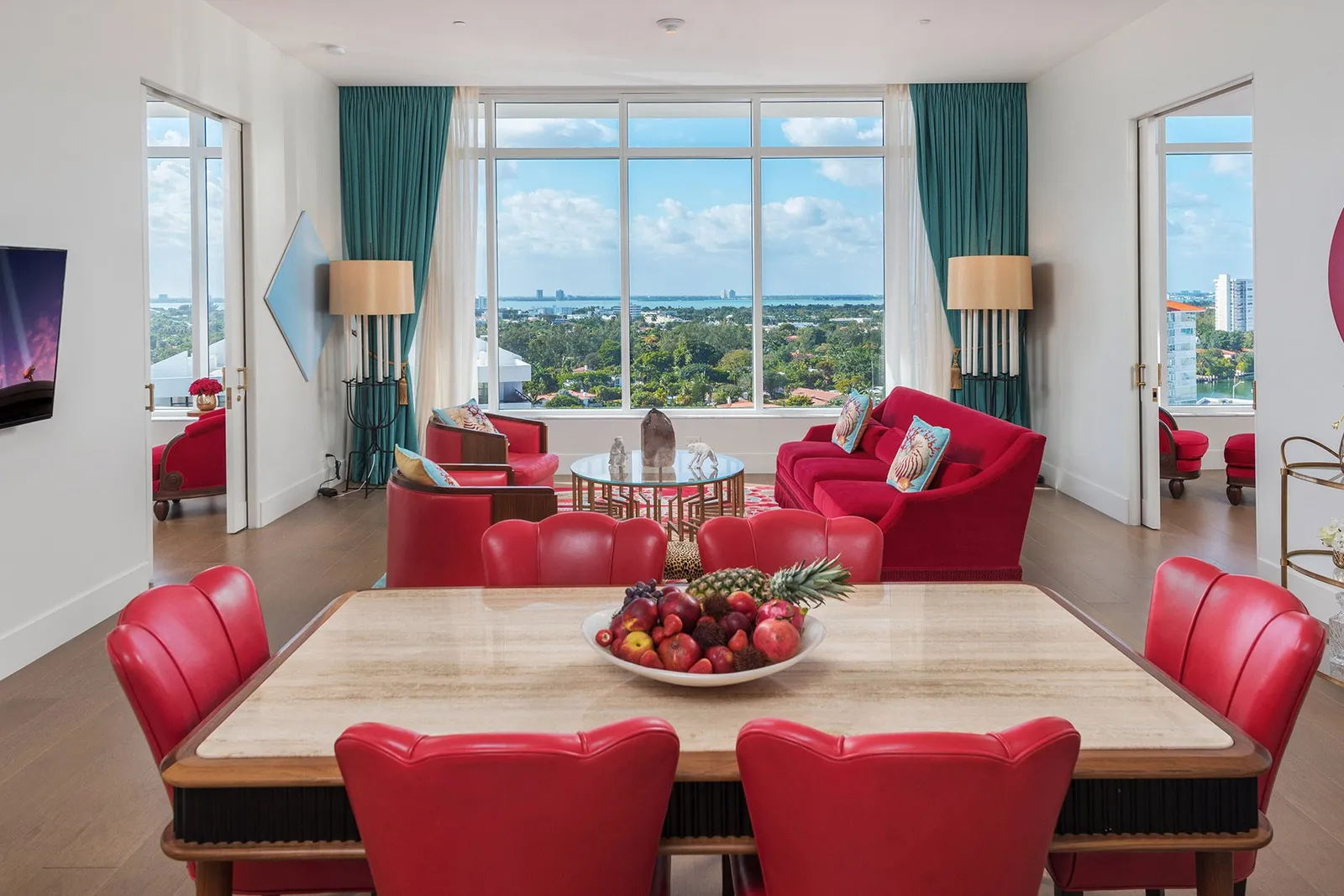 The Bay View Two Bedroom Suite: the dining table with red chairs, the living room and the window towards the bay.