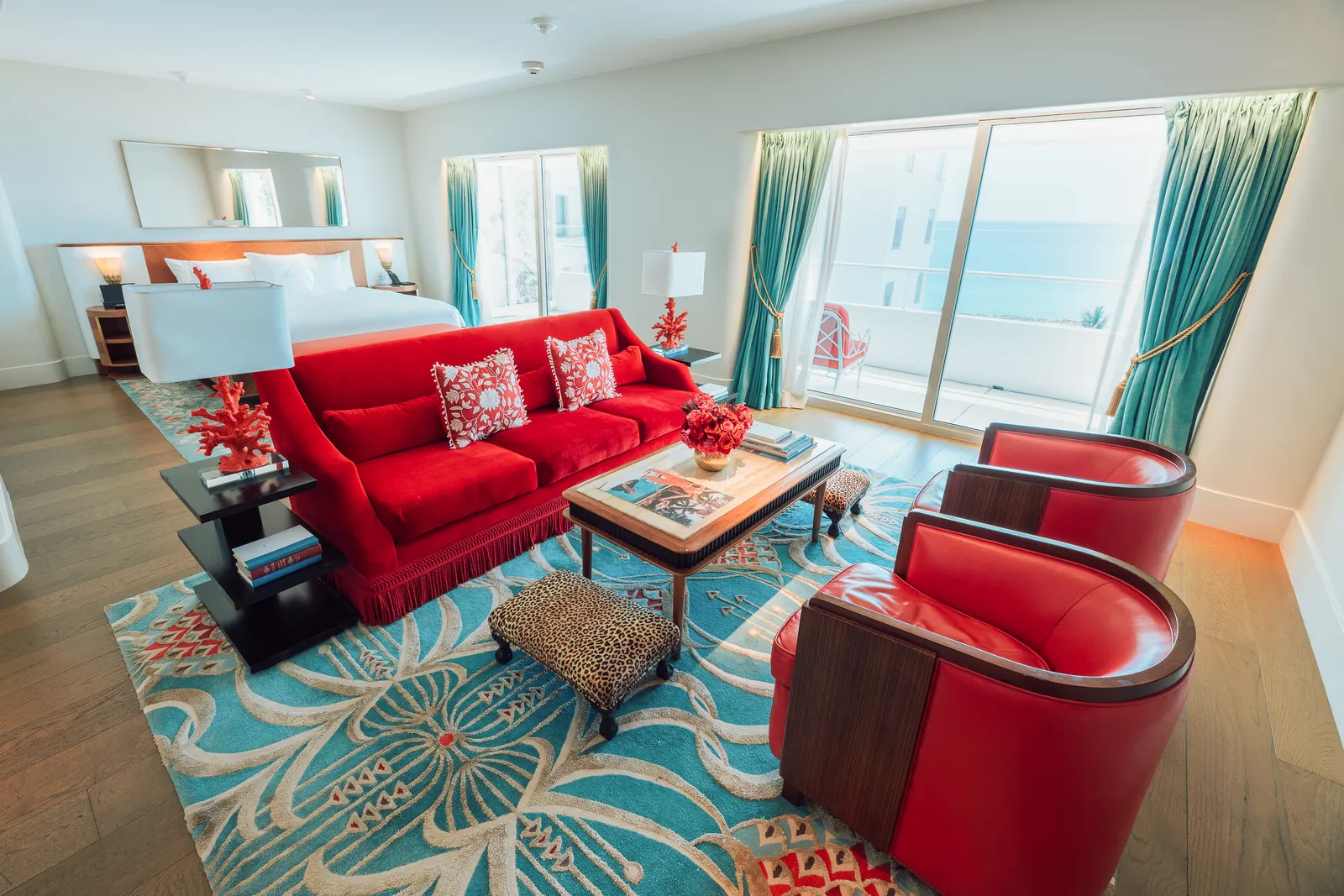 The Ocean View Junior Suite: red sofa and armchairs, a turquoise carpet and the windows onto the ocean.