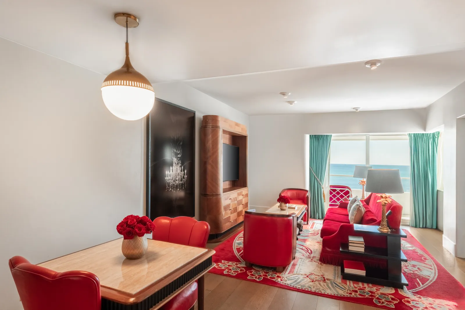 The Ocean View Suite’s living room: red armchairs, the dining table, a globe lamp and the ocean in the windows.