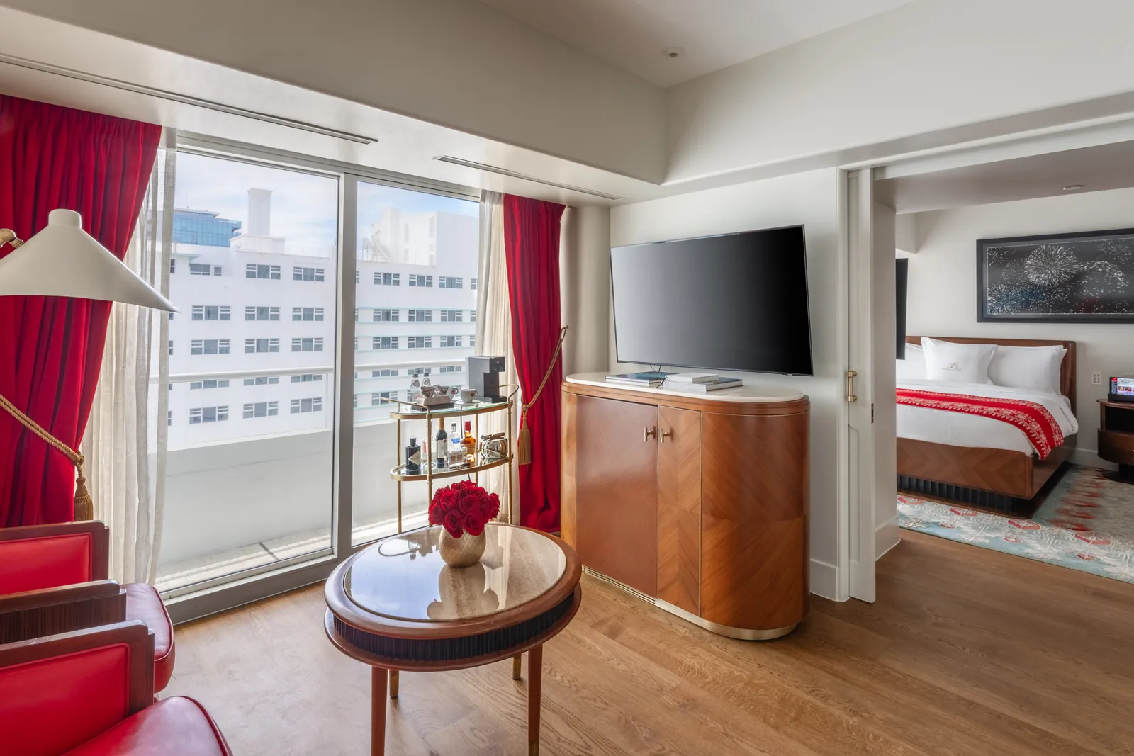 The junior suite with 2 queen beds: the round table with red chairs, the television cabinet and the beds beyond.